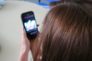 Foto einer Person von hinten, hält ein Smartphone in der Hand