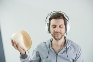 Eine Person mit geschlossenen Augen trägt Kopfhörer und hält eine Muschel in der Handt