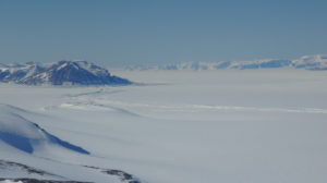 Blick auf das George-IV Ice Shelf, welches zwischen Alexander Island (Vordergrund) und der westl. Antarktischen Halbinsel (Hintergrund) eingespannt ist. Der markante Spaltenbogen markiert die Aufsetzlinie, den Übergang zwischen Zuflussgletscher und schwimmendem Schelfeis. Aufgenommen während eines NASA IceBridge Messfluges am 16. November 2011. Photo: Matthias Braun.