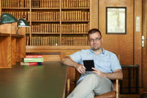 Dr. Axel Kuhn sitzt, mit einem elektronischen Lesegerät in der Hand, vor einem Bücherregal