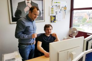 Herr Kiel und Herr Müller betrachten zwei Computerbilgschirme