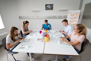 Vier Studierende und ein Tutor sitzen an einem Tisch und nähen etwas.