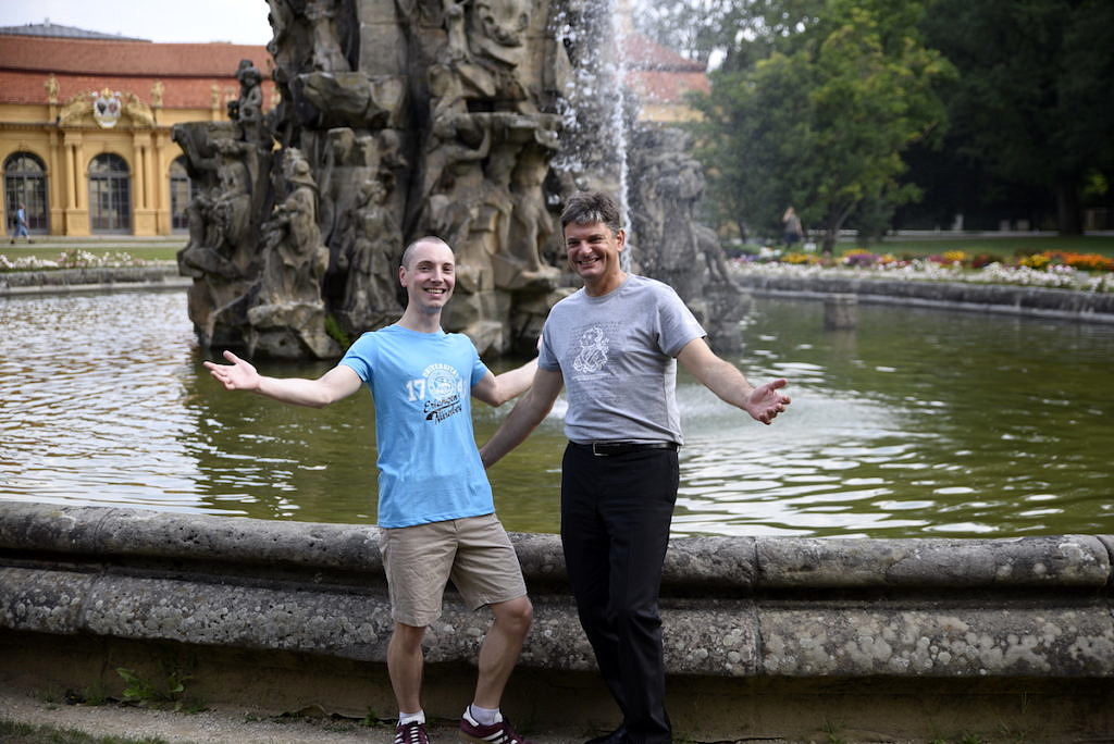 Prof. Dr. Joachim Hornegger und ein Student stehen in den neuen FAU-Shirts vor dem Schlossbrunnen.