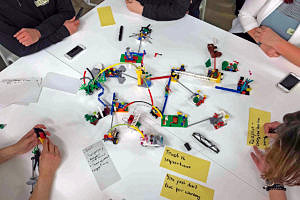 Auf einem Tisch bauen Personen ein Modell mit Lego-Männchen und Karteikarten