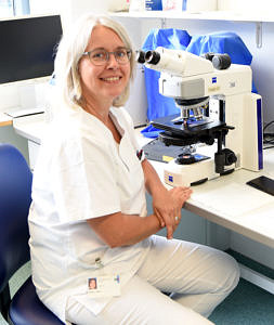 Kerstin Poller sitzt an ihrem Arbeitsplatz. Neben ihr steht ein Mikroskop.