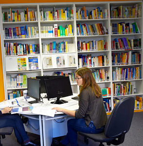 Studentin, die am Tisch lernt und im Hintergrund die Bibliothek