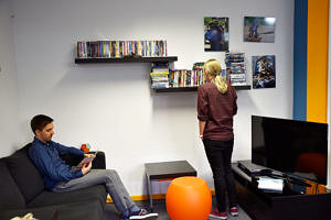 Blick auf die Sofaecke: Ein Student sitzt auf der Couch und liest; eine andere Studentin schaut sich die Videos an