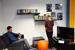 One student is sitting on a couch reading, another is looking at videos.