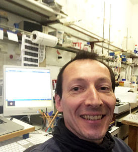 Selfie von Christian Emilius: Im Hintergrund sieht man seinen PC und ein paar Arbeitmaterialien eines Labors.