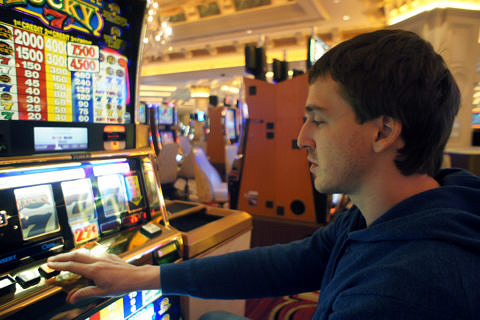 Junger Mann sitzt vor Spielautomat im Kasino.