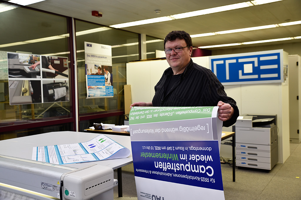 Christian Gath hält ein DinA1-Plakat in den Handen und blickt in die Kamera.