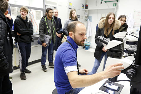 Schüler hinter Forscher mit Mirkoskop