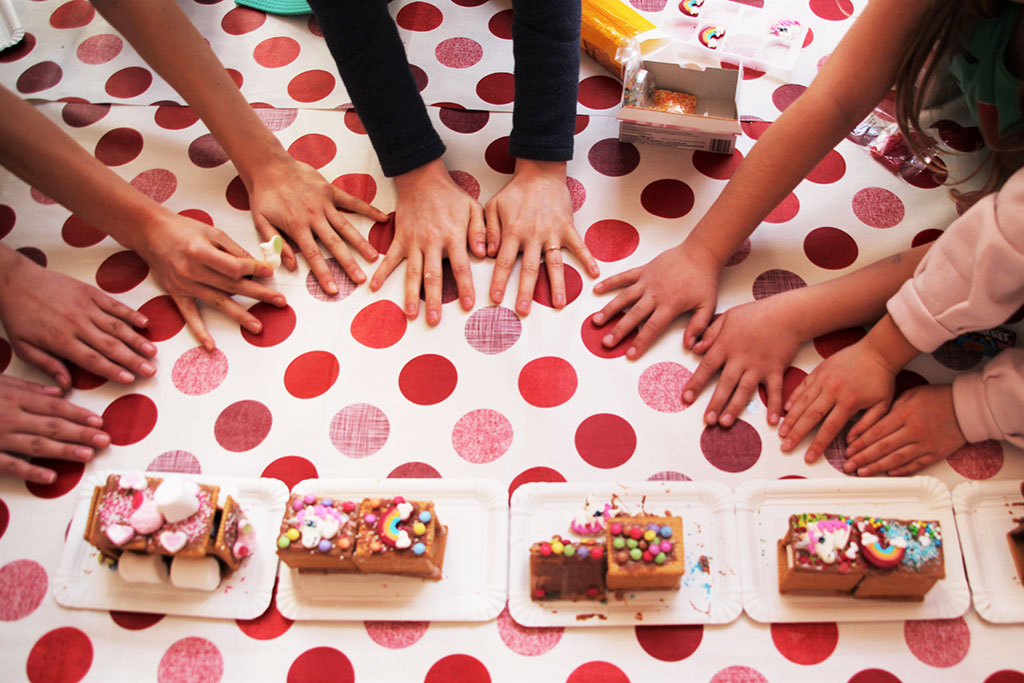 Oberhalb des Bildes sind Kinderhände abgebildet. Unterhalb des Bildes Süßigkeiten (Kekse, Marshmallows, Gummibärchen), die Zugwagons ähneln. Der Untergrund ist weiß mit roten Punkten.