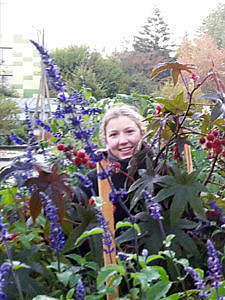 Das Gesicht einer Frau ragt zwischen Blättern und lilafarbenen Blumen hervor.