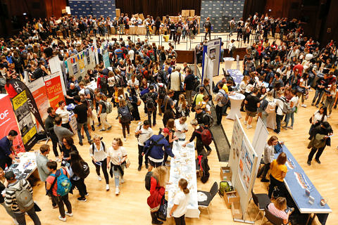 Eine große Halle mit vielen Studierenden und Infoständen.