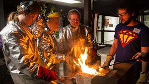 Vier Menschen stehen in Schutzanzügen an einem Feuer.