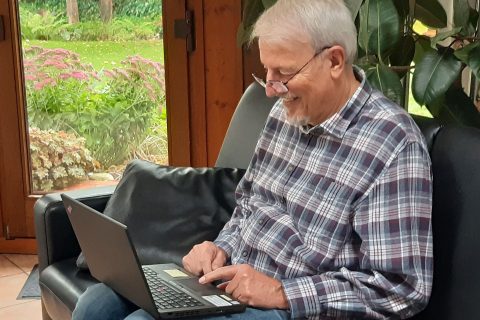 Mann sitzt auf Sofa mit Laptop auf dem Schoss.