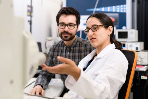Eine Wissenschaftlerin zeigt ihrem Kollegen etwas am Elektronenmikroskop.