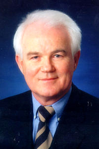Portraitbild eines älteren Mannes mit weißem Haar im Anzug vor einem blauen Hintergrund