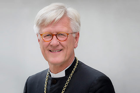 Portraitbild eines älteren Mannes mit Brille, weißen Haaren und in einem Bischofsumhang gekleidet; der Hintergrund ist grau