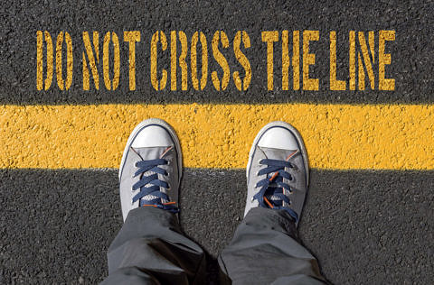 "Do not cross the Line" Schriftzug auf einer Straße und zwei Shuhe davor