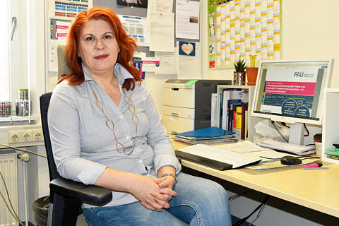 Eine Dame mit roten Haaren sitzt an ihrem Arbeitsplatz und blickt in die Kamera.