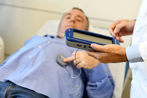 Ein Mann hält sich ein Programmiergerät an den Bauch, ein Arzt steuert damit den Schrittmacher.