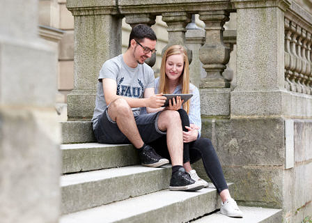 Studierende sitzen auf einer Treppe und schauen in ein Tablet.