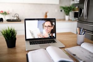 Schreibtisch mit Laptop, auf dem eine Frau in einem Videoanruf etwas erklärt