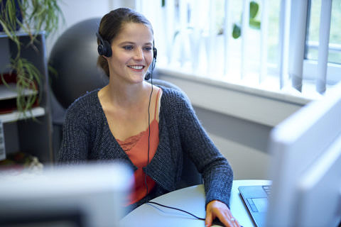 Frau vor einem Computer mit Headset.