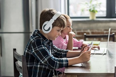 Zwei Kinder sitzen am Esstisch an Laptop und Tablet.