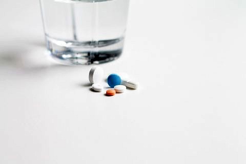 Tabletten und ein Glas Wasser auf einem Tisch.