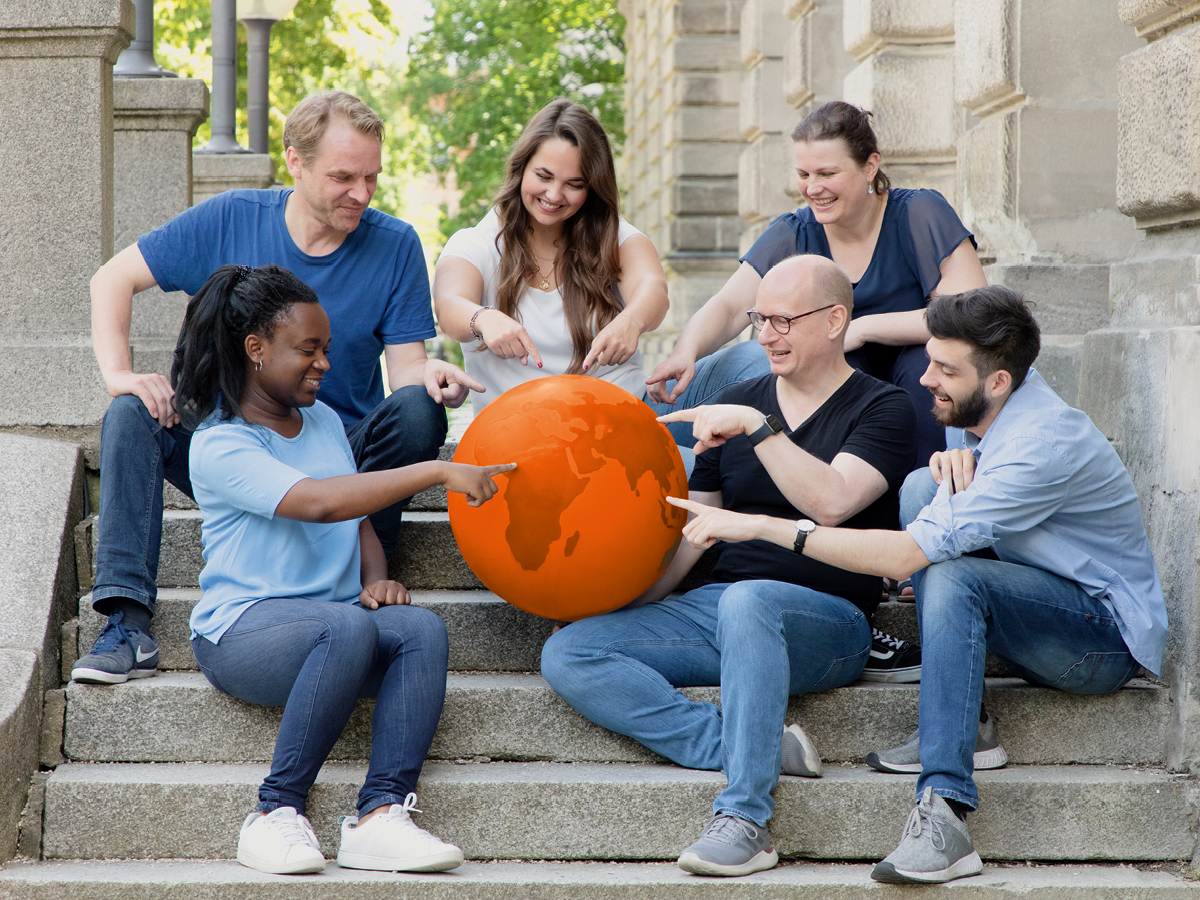 Menschen sitzen um einen Globus und zeigen mit ihren Fingern darauf