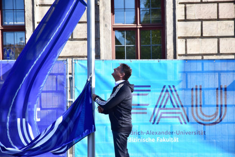 Präsident Prof. Dr. Joachim Hornegger hisst vor dem Erlanger Schloss eine Fahne mit dem neuen FAU Logo.