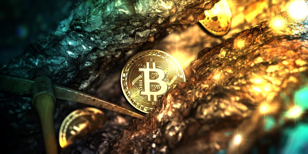Bitcoin-Münze mit Spitzhacke zwischen Goldbrocken.
