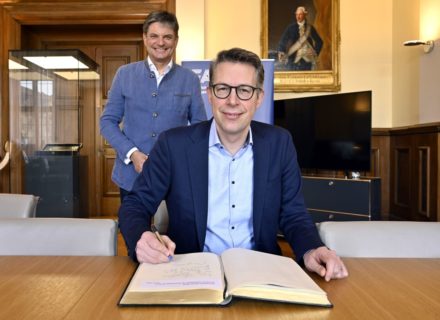 Staatsminister Markus Blume trägt sich ins Buch ein, hinter ihm steht Joachim Hornegger, FAU-Präsident