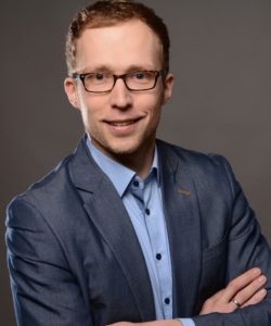 Man with short brown hair, glasses and wearing a suit