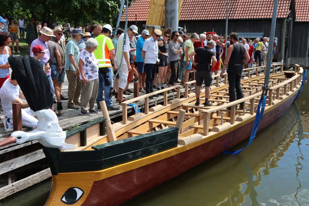 Menschen an Land neben Römerboot in Wasser