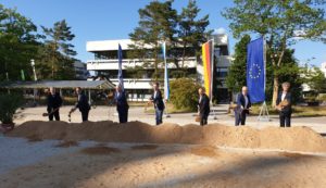Männer mit Spaten vor Erdhügel im Hintergrund Flaggen der FAU, Bayerns, Deutschlands, Europas