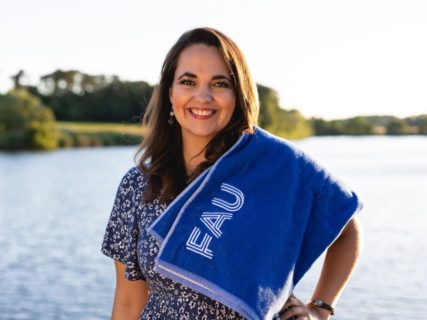Frau mit blauem Handtuch mit FAU-Logo vor Wasser