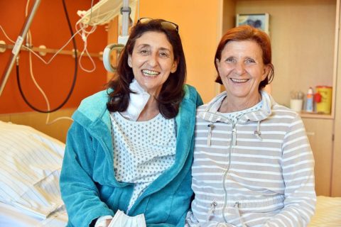 Zwei Frauen sitzen auf einem Krankenhausbett, eine hat einen Verband am Hals