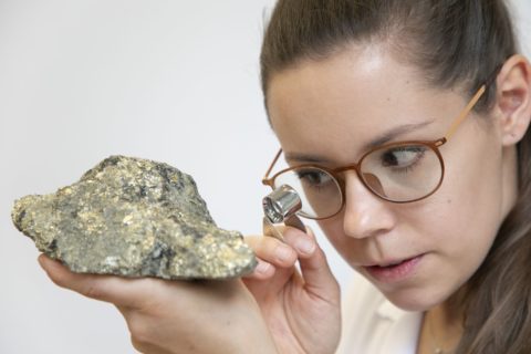 Irina Kirchberger, Doktorandin Mineralogie an der NatFak schaut mit Lupe auf Stein