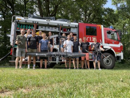 Das Team steht gemeinsam mit den beiden Drohnen vor einem Feuerwehrauto