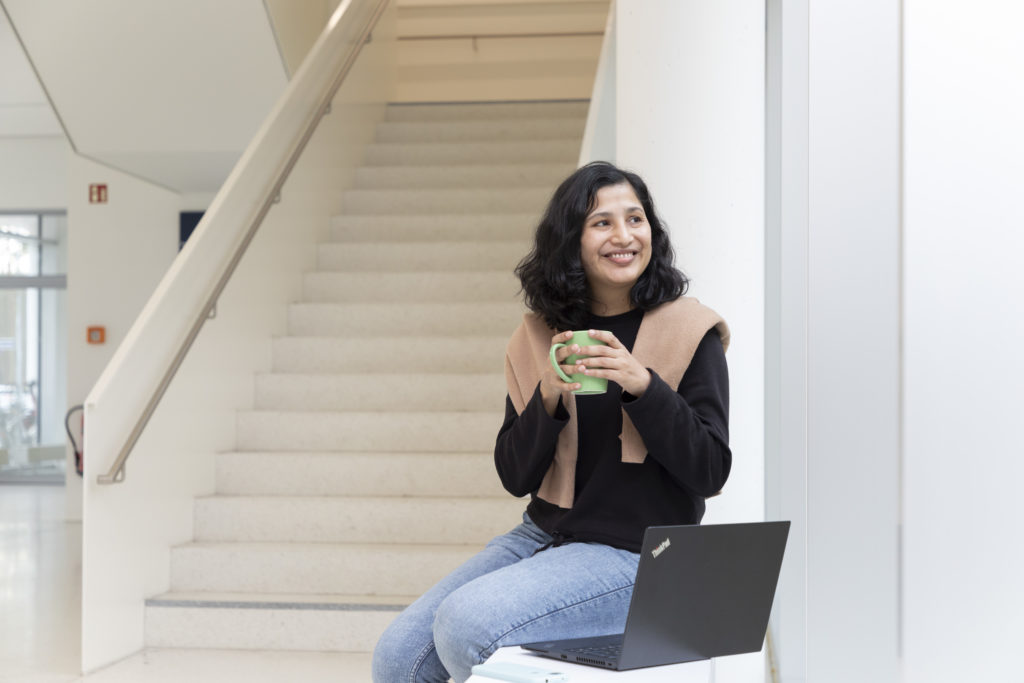 Eine Frau sitzt an einer Treppe und hat eine Tasse in der Hand.