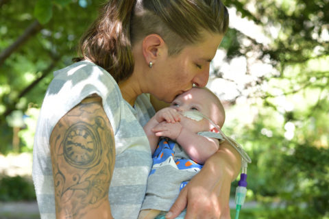Eine Frau hält ihr Baby im Arm und gibt ihm einen Kuss auf die Stirn.