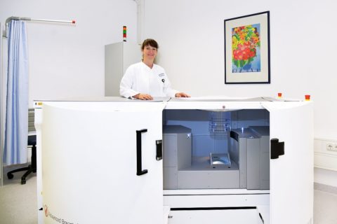 Eine Ärztin steht hinter einem großen weißen CT-Gerät.