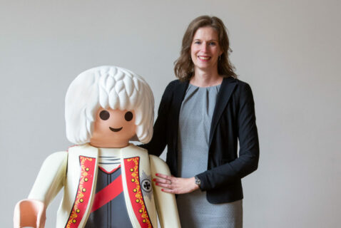 Frau steht neben Playmobil-Figur.