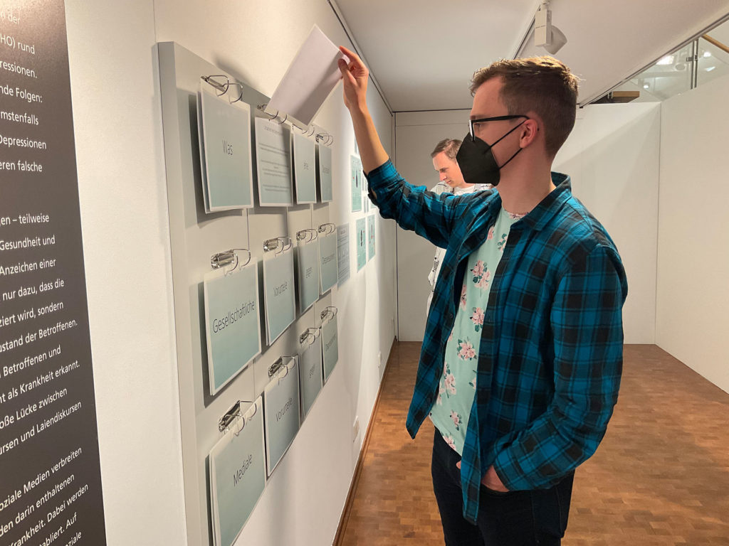 Zwei Männer schauen sich in einer Ausstellung Texttafeln an.