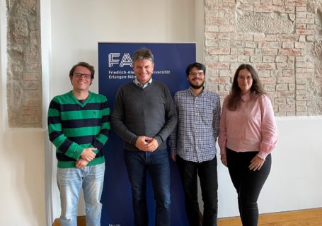 Der FAU-Präsident steht zusammen mit den drei neuen Gewinner:Innen des President's Welcome Award vor einem FAU-Banner.