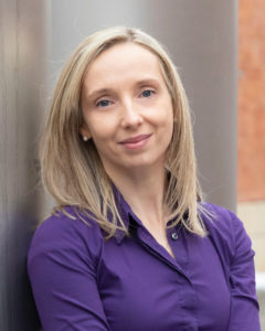 A woman with long blond hair and a purple blouse.